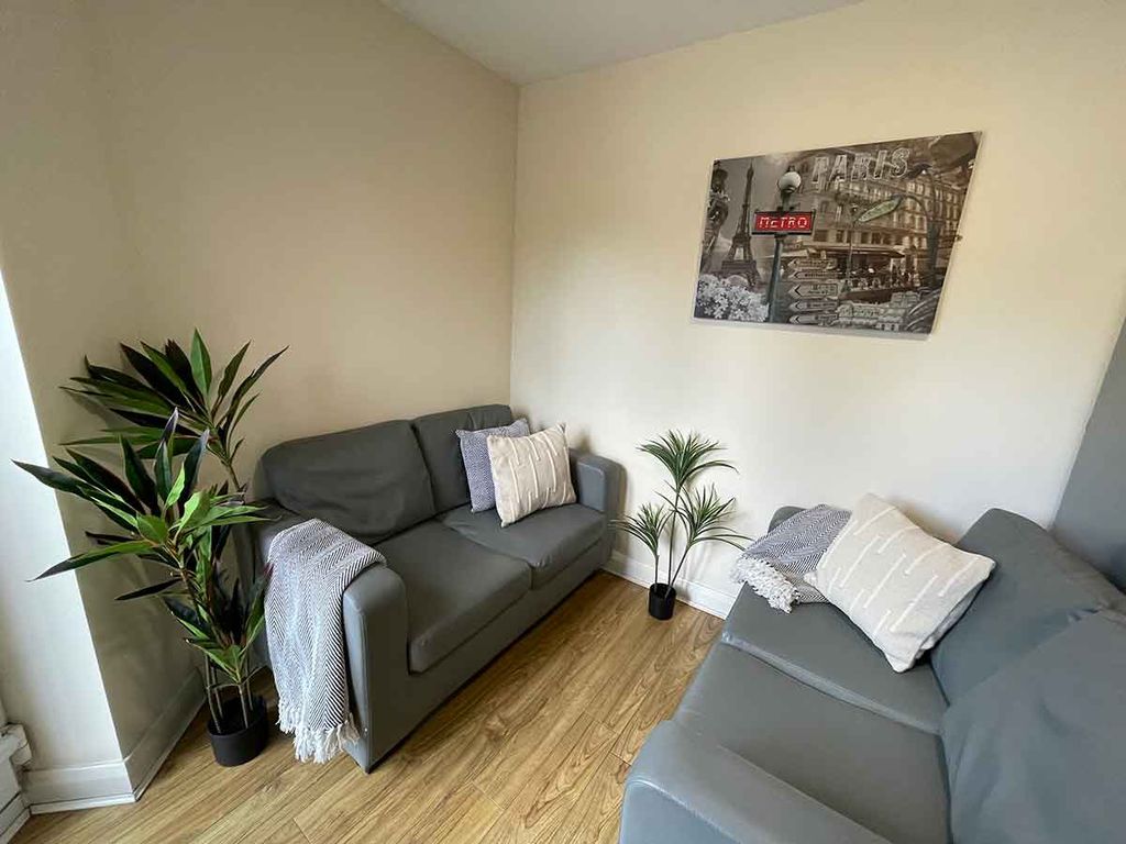 A cozy living room corner with two gray sofas, decorative pillows, a potted plant, and a wall art piece on a light-colored wall.