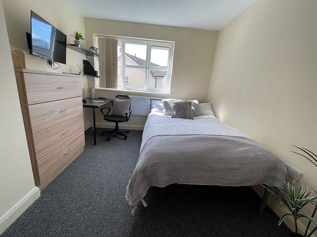 A tidy bedroom with a single bed, desk, chair, wall-mounted TV, and a chest of drawers. A window lets in natural light.