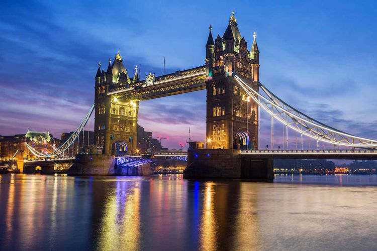 Tower Bridge illuminated at dusk, reflecting on the Thames with a vibrant blue and purple sky in the background.