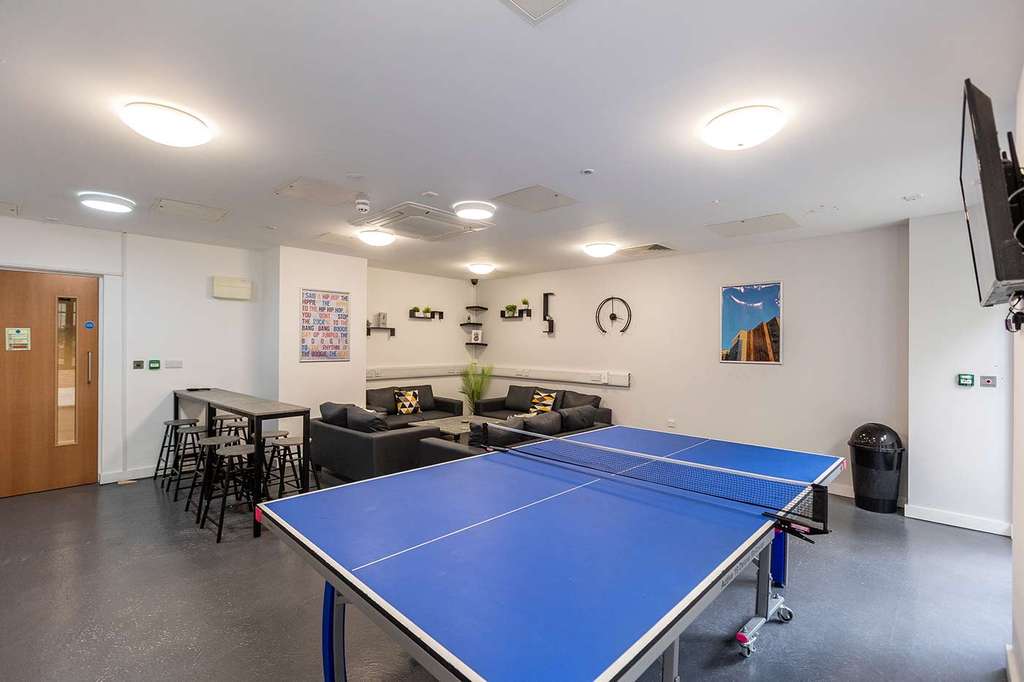 Room with a ping pong table, sofas, wall art, and a wall-mounted TV. Bright lighting and minimalist decor create a relaxed atmosphere.