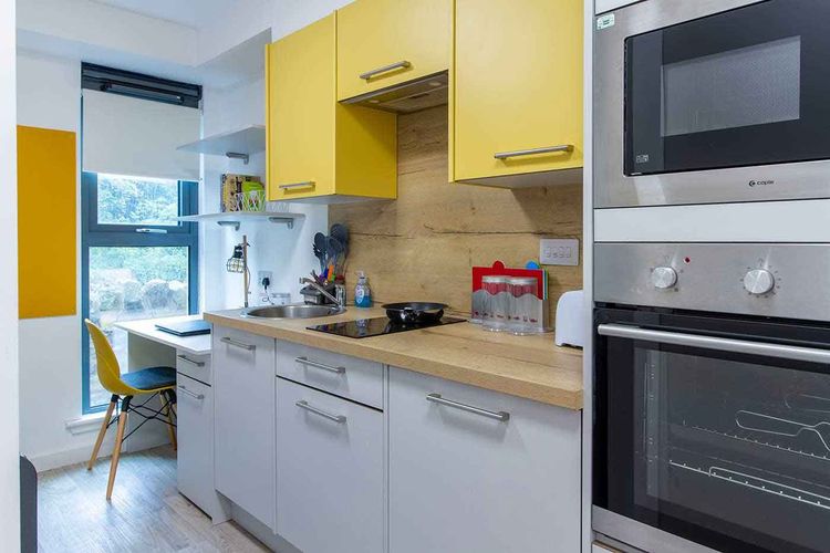 Modern kitchen with yellow cabinets, a built-in oven, microwave, and a small dining area by a large window with a yellow chair.