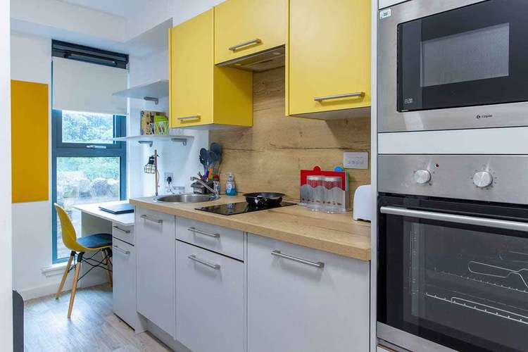 Modern kitchen with yellow cabinets, a built-in oven, microwave, and a small dining area by a large window with a yellow chair.