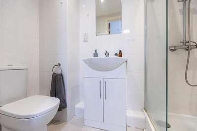 Modern bathroom with white tiles, featuring a toilet, sink with cabinet, mirror, towel rack, and glass-enclosed shower.