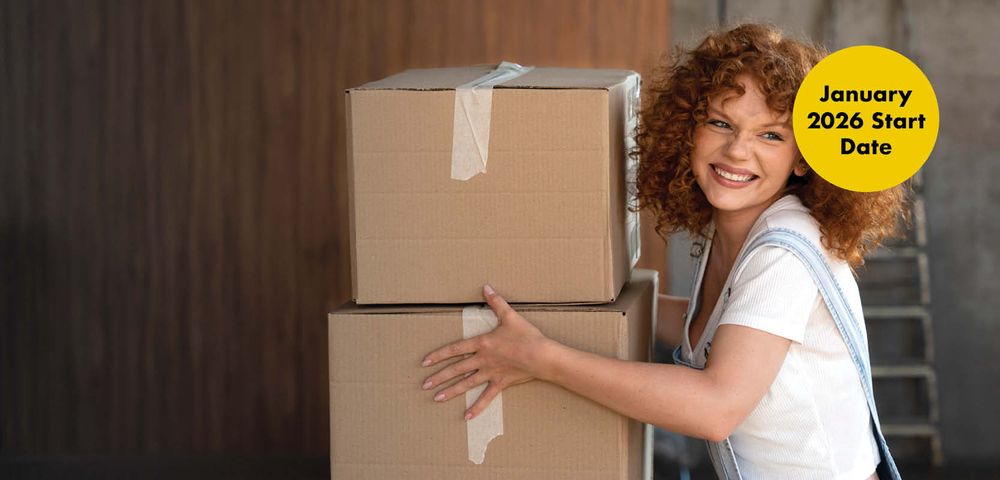 Smiling woman with curly hair holding two cardboard boxes, wearing overalls. Yellow circle reads "January 2026 Start Date."