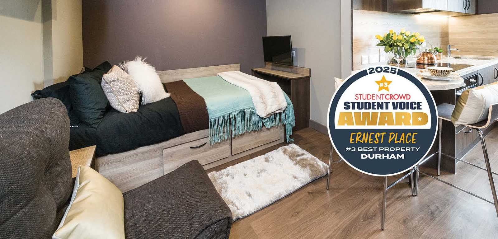 A modern kitchen with a small dining area, two stools, and a flower vase. A "Student Voice Award" badge is displayed above.