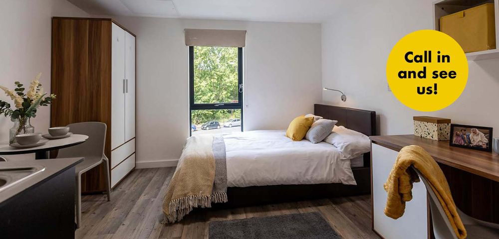 Cozy bedroom with a bed, pillows, wardrobe, and a small dining area. Large window with a view of greenery. Text bubble: "Call in and see us!"