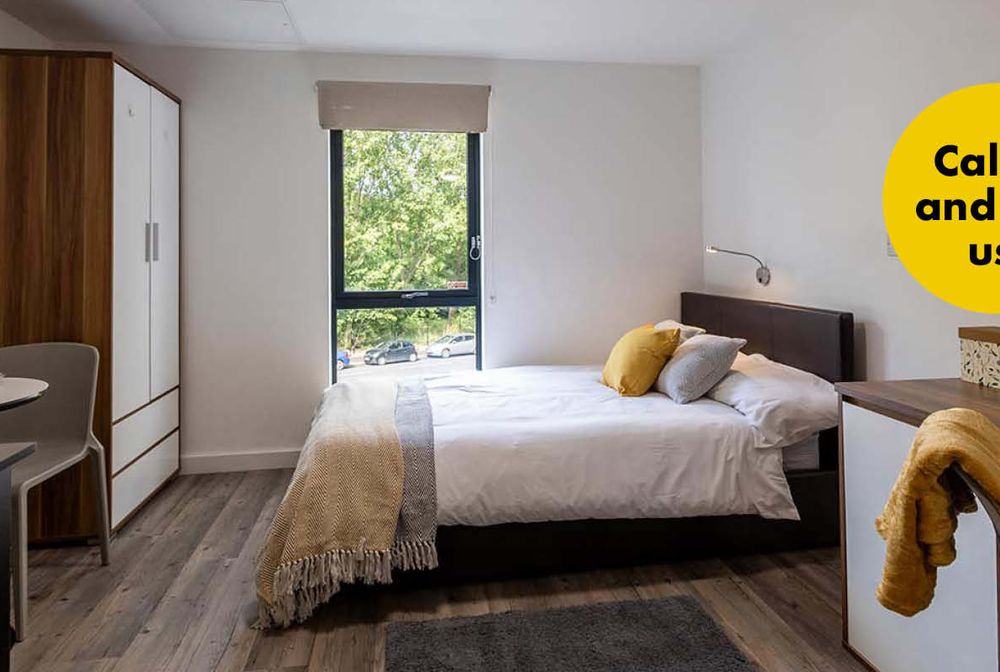 Cozy bedroom with a bed, pillows, wardrobe, and a small dining area. Large window with a view of greenery. Text bubble: "Call in and see us!"