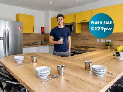 Man holding a coffee cup in a modern kitchen with yellow cabinets. "Flash Sale £129pw" logo in top right corner.