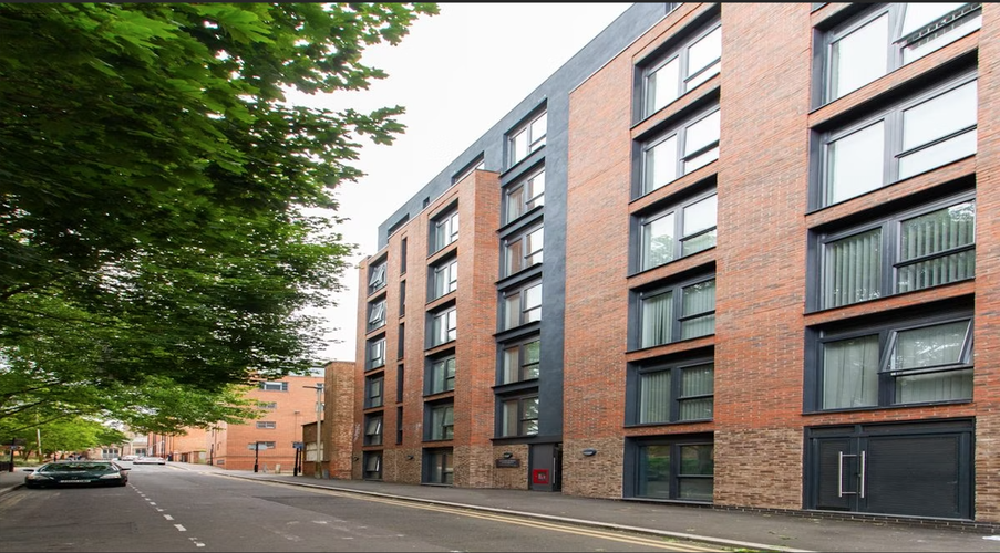 A modern, multi-story brick apartment building with large windows on a tree-lined street.