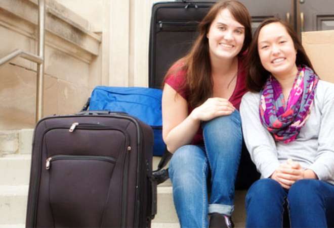 Two students sitting next to suitcases