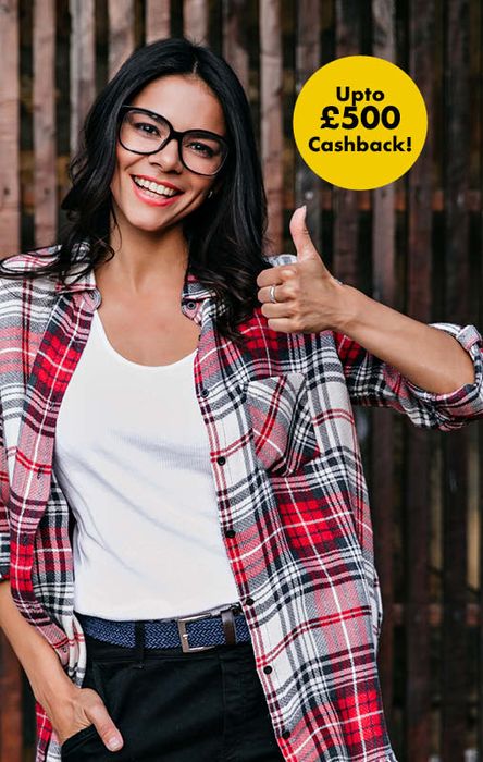 Smiling woman in glasses and plaid shirt gives thumbs up. Text bubble reads "Up to £500 Cashback!" against a wooden background.
