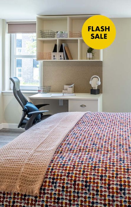 Modern bedroom with a desk, chair, and shelving. A "Flash Sale" sign is on the wall. The bed has a colorful polka dot cover.