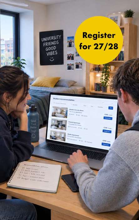 Two people sit in a cozy room, browsing student accommodations on a laptop. A sign reads "Register for 27/28." A notebook and bottle are on the table.
