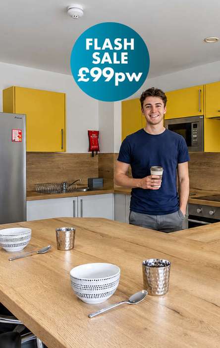 Man in a kitchen holding a coffee cup, with a flash sale offer of £99 per week displayed, yellow cabinets, and wooden countertops.