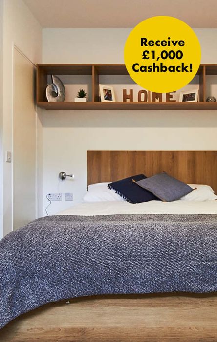 Bedroom with a wooden bed, blue-gray bedding, and shelves with decor. A yellow circle in the corner reads "Receive £1,000 Cashback!".