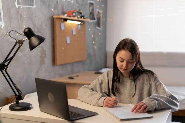 Student writing notes on desk in student accommodation