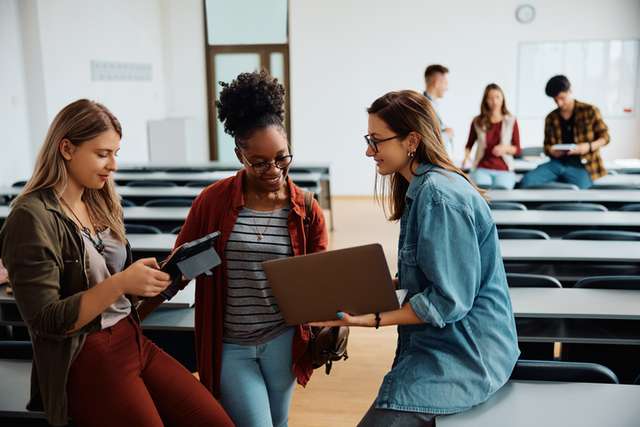 Happy female students using wireless technology in lecture hall
