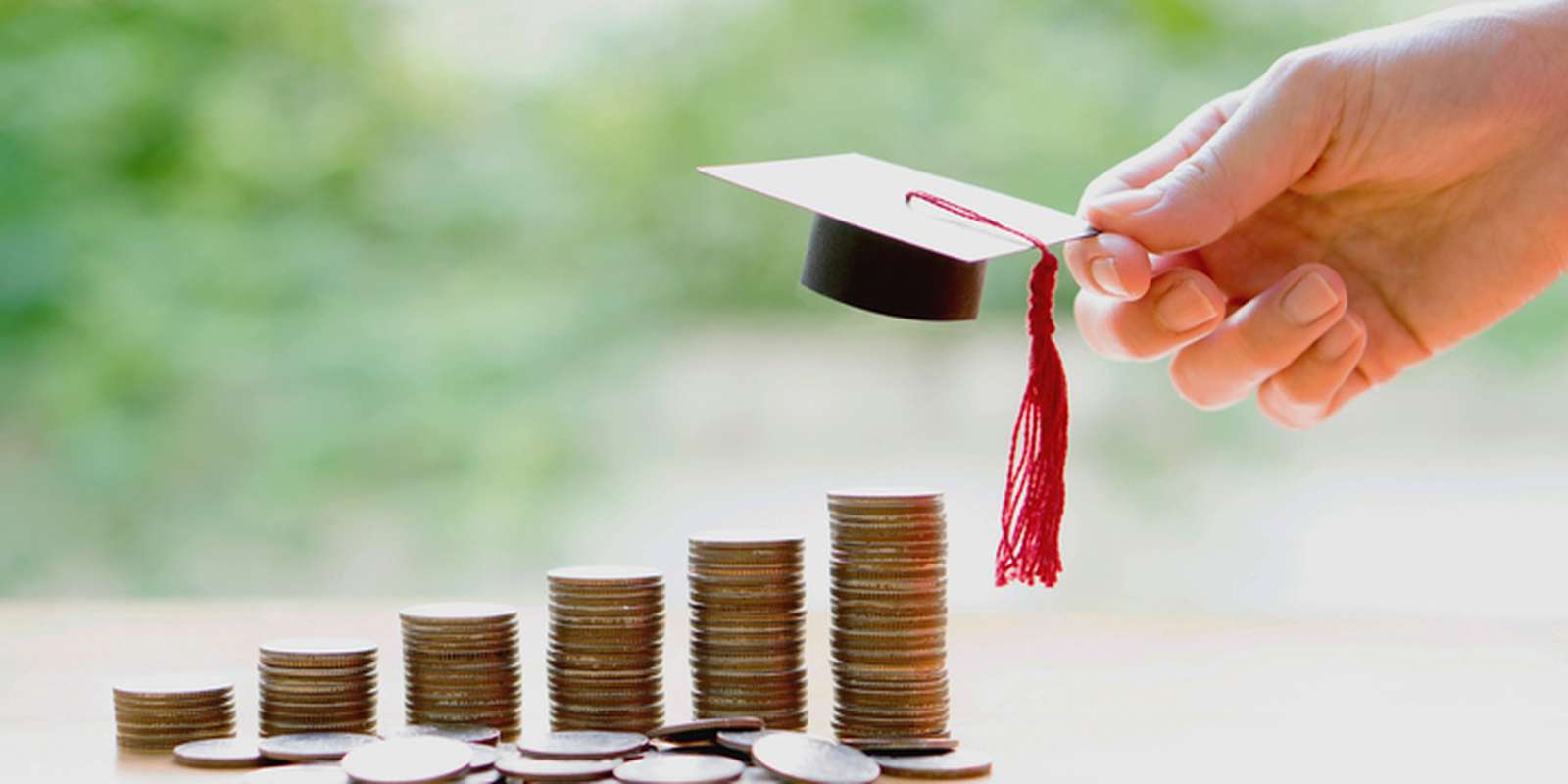 A person holding a small university hat above a stack of coins