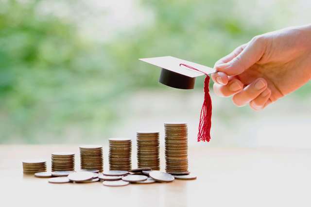 A person holding a small university hat above a stack of coins
