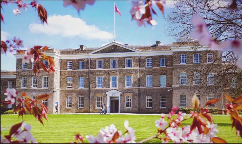 Historic brick building with a central pediment, surrounded by blooming cherry blossoms and a green lawn under a blue sky.