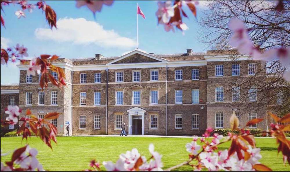 Historic brick building with a central pediment, surrounded by blooming cherry blossoms and a green lawn under a blue sky.