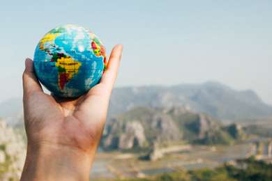 Holding up a small world globe with a scenic mountain background