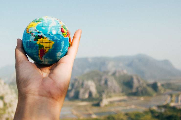 Holding up a small world globe with a scenic mountain background