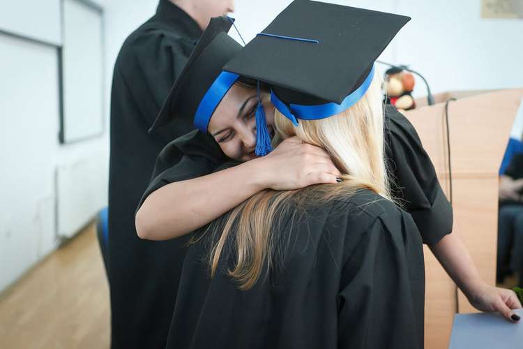 Two students graduating and hugging