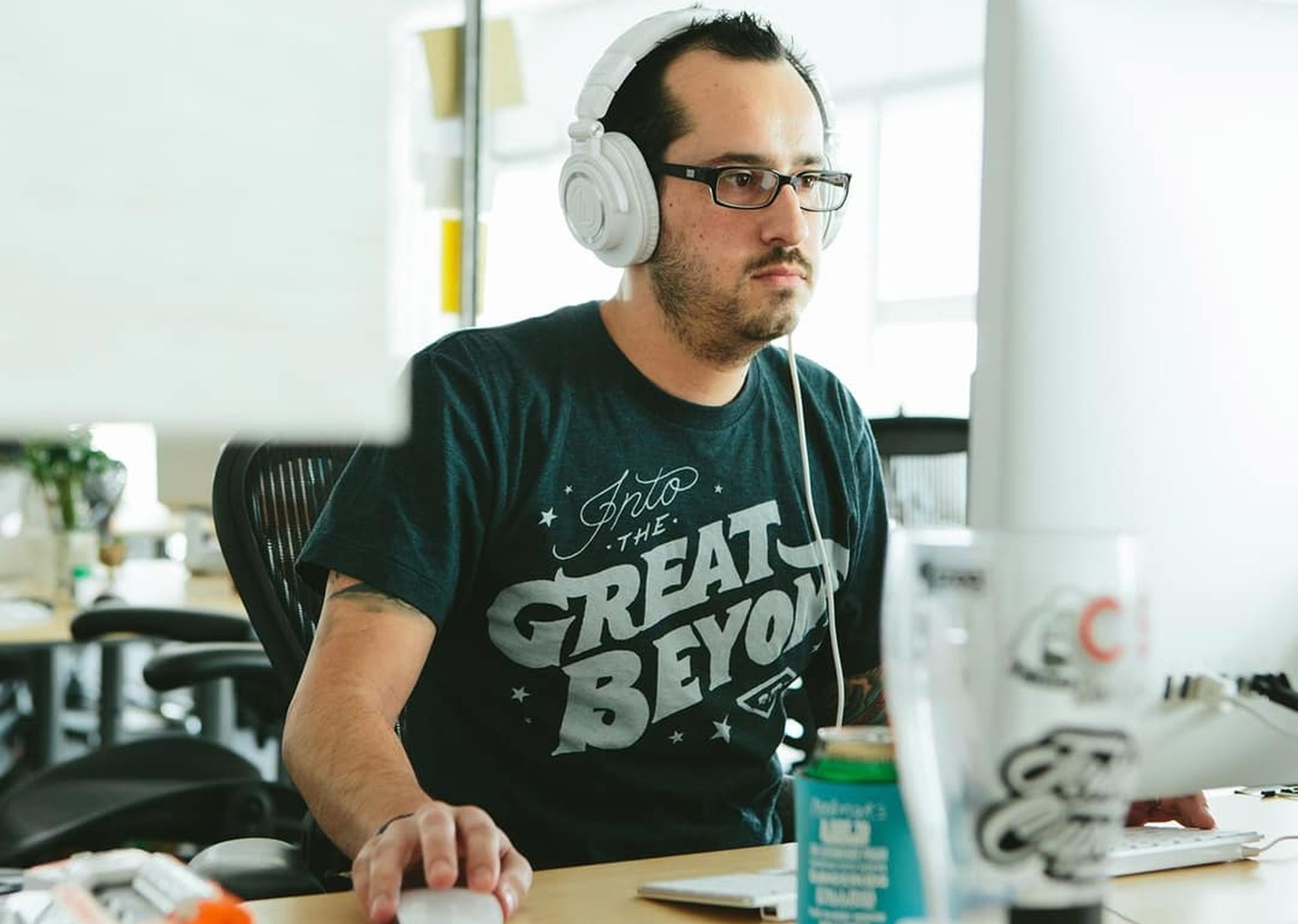 A man works at a desk wearing a custom t-shirt that says "into the great beyond"