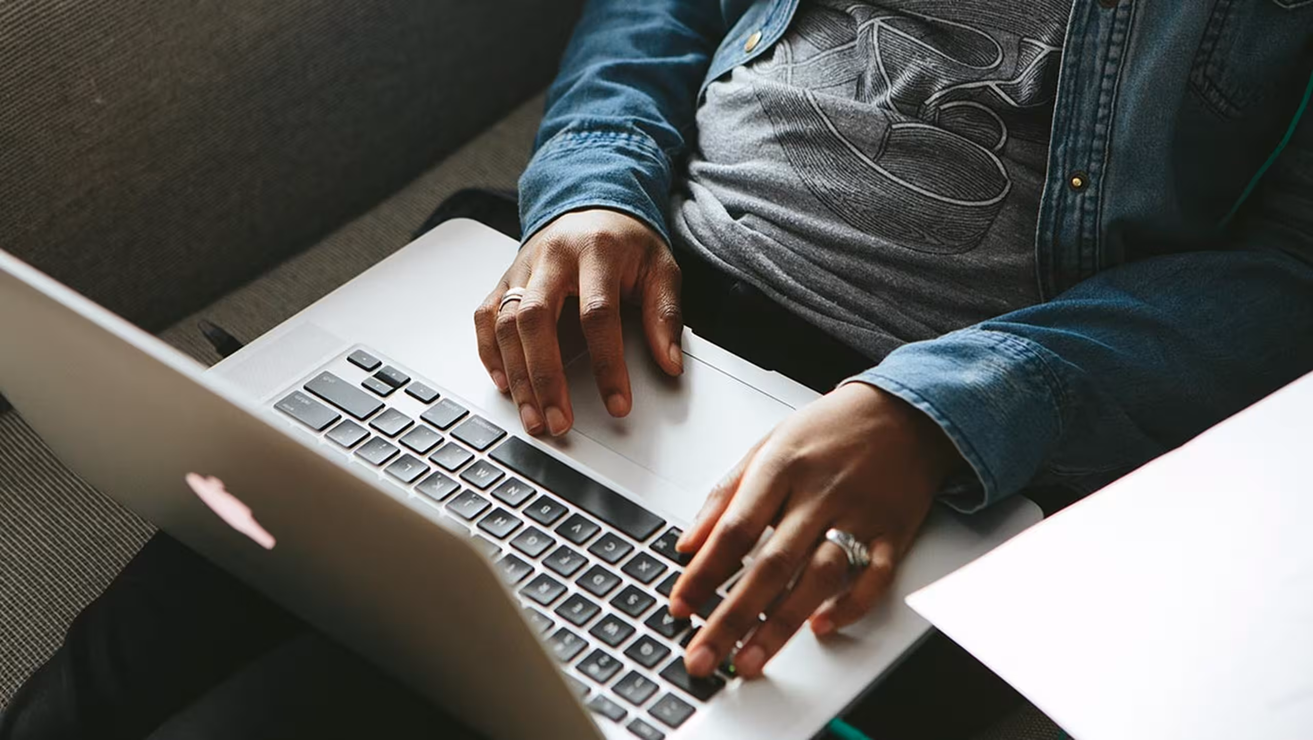 A man wearing a t-shirt works on his couch with his laptop 