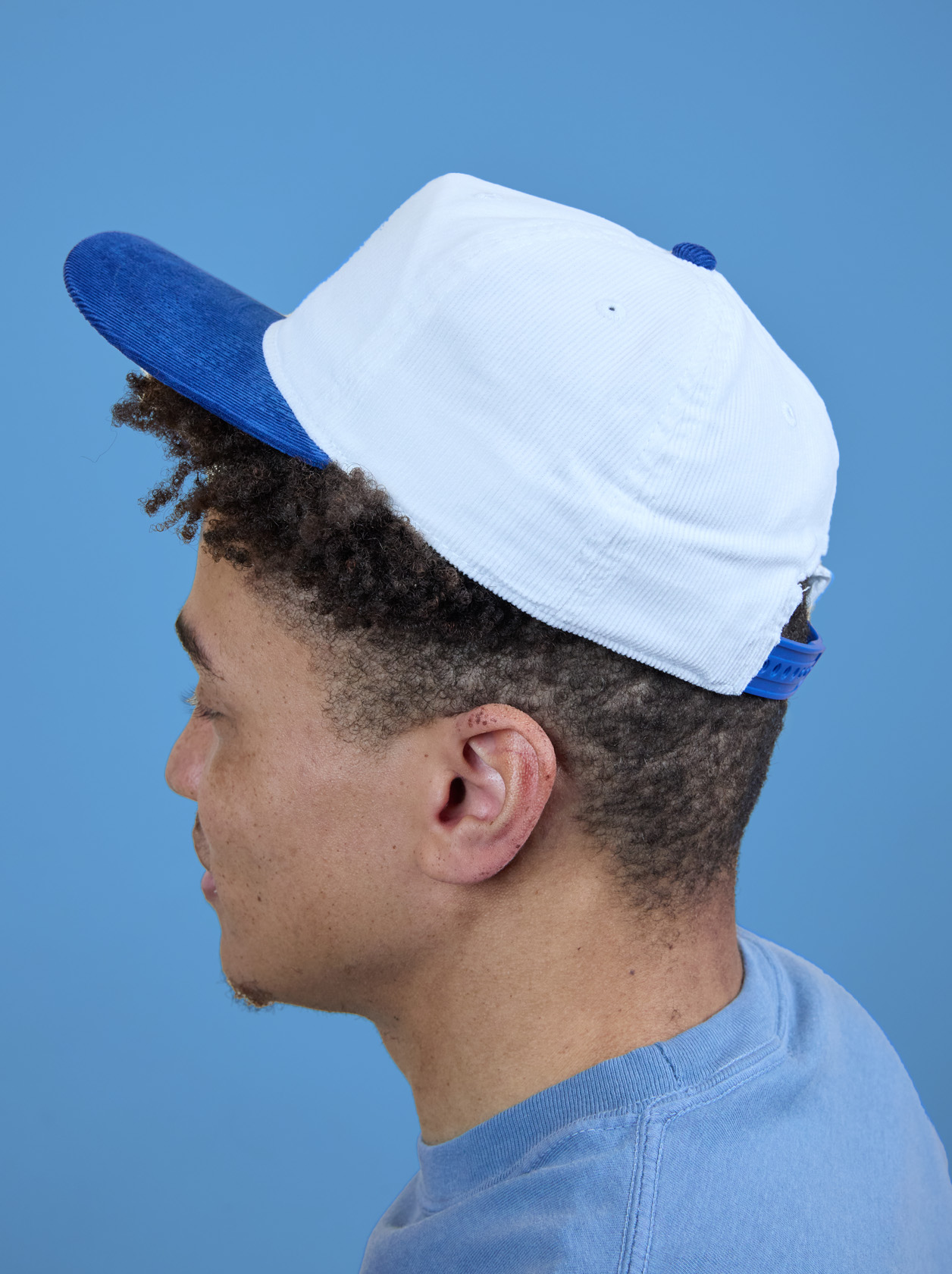 Person wearing a white and blue baseball cap, facing left, against a blue background.