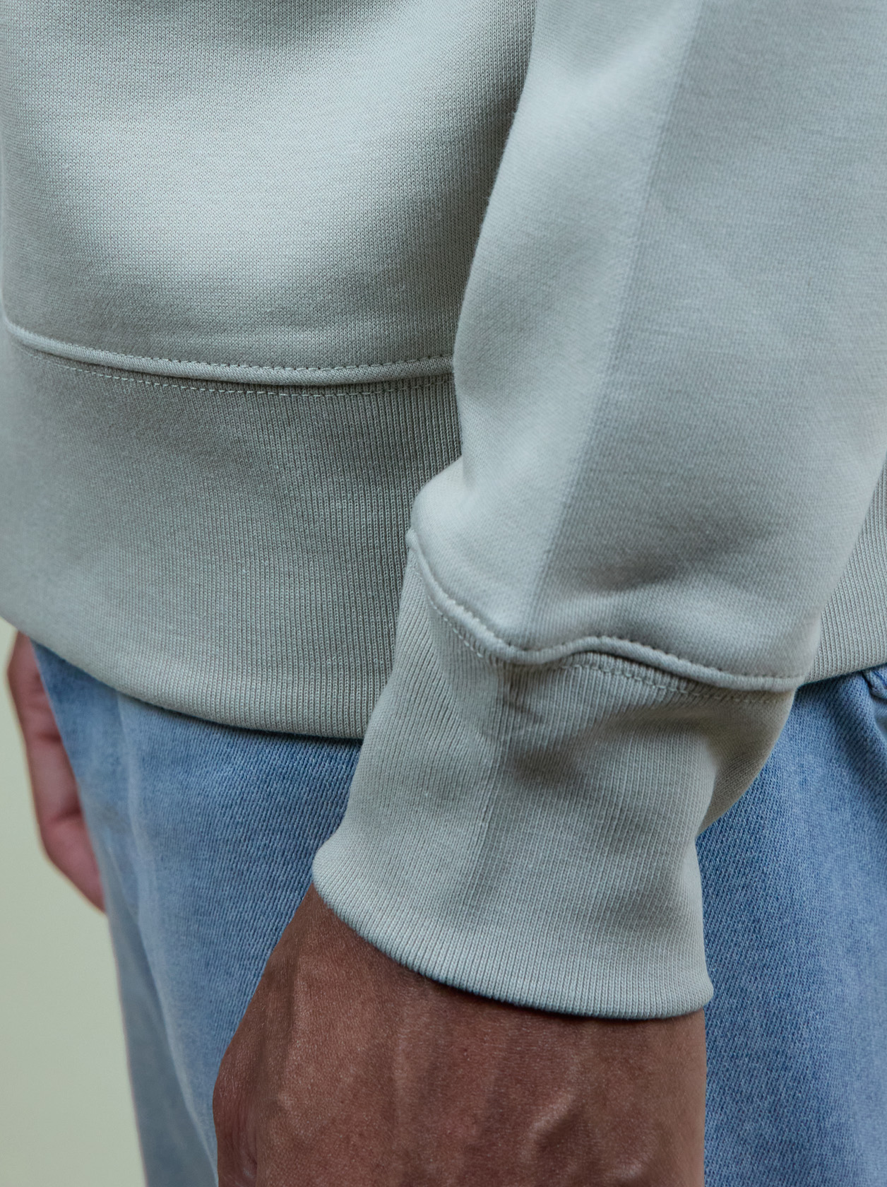 Close-up of a person wearing a light gray sweatshirt and blue jeans, with a focus on the sleeve and hand.