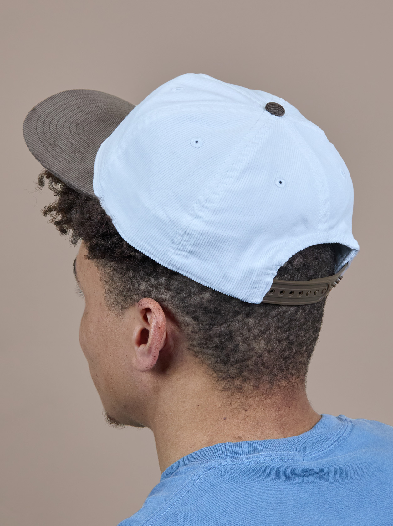 Person wearing a backward white and brown cap and a blue shirt, facing away against a plain background.