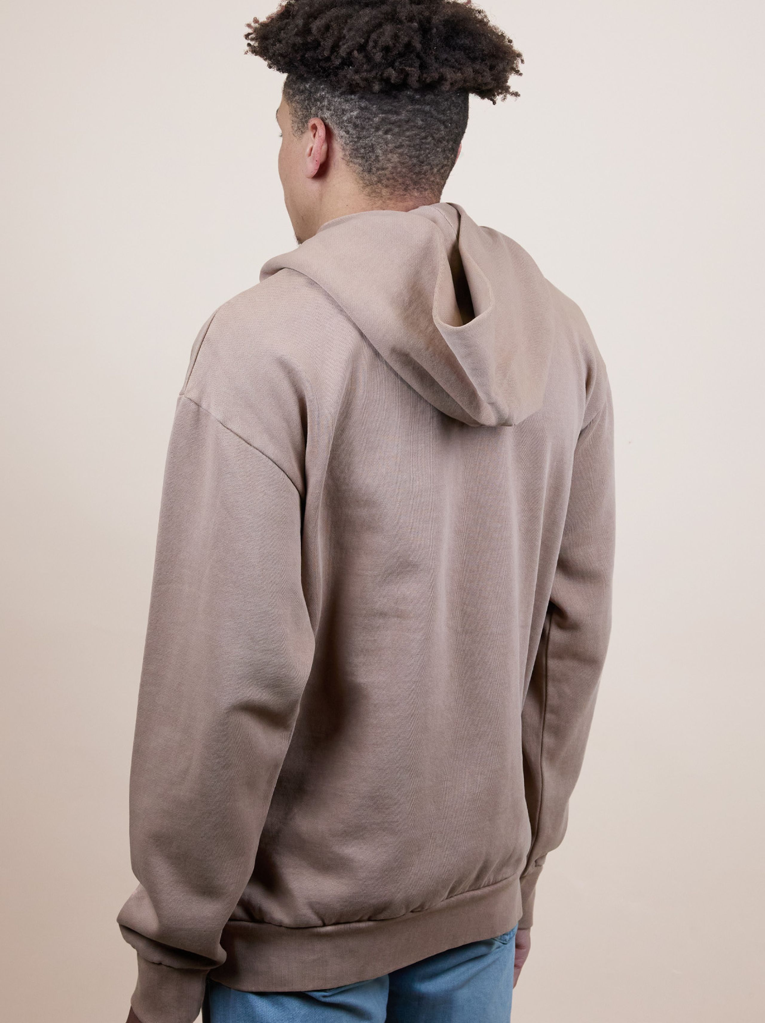 Person wearing a brown hoodie and blue jeans, facing away from the camera against a plain background.