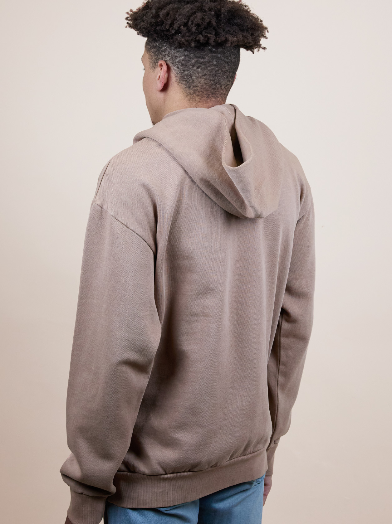 Person wearing a brown hoodie and blue jeans, facing away from the camera against a plain background.