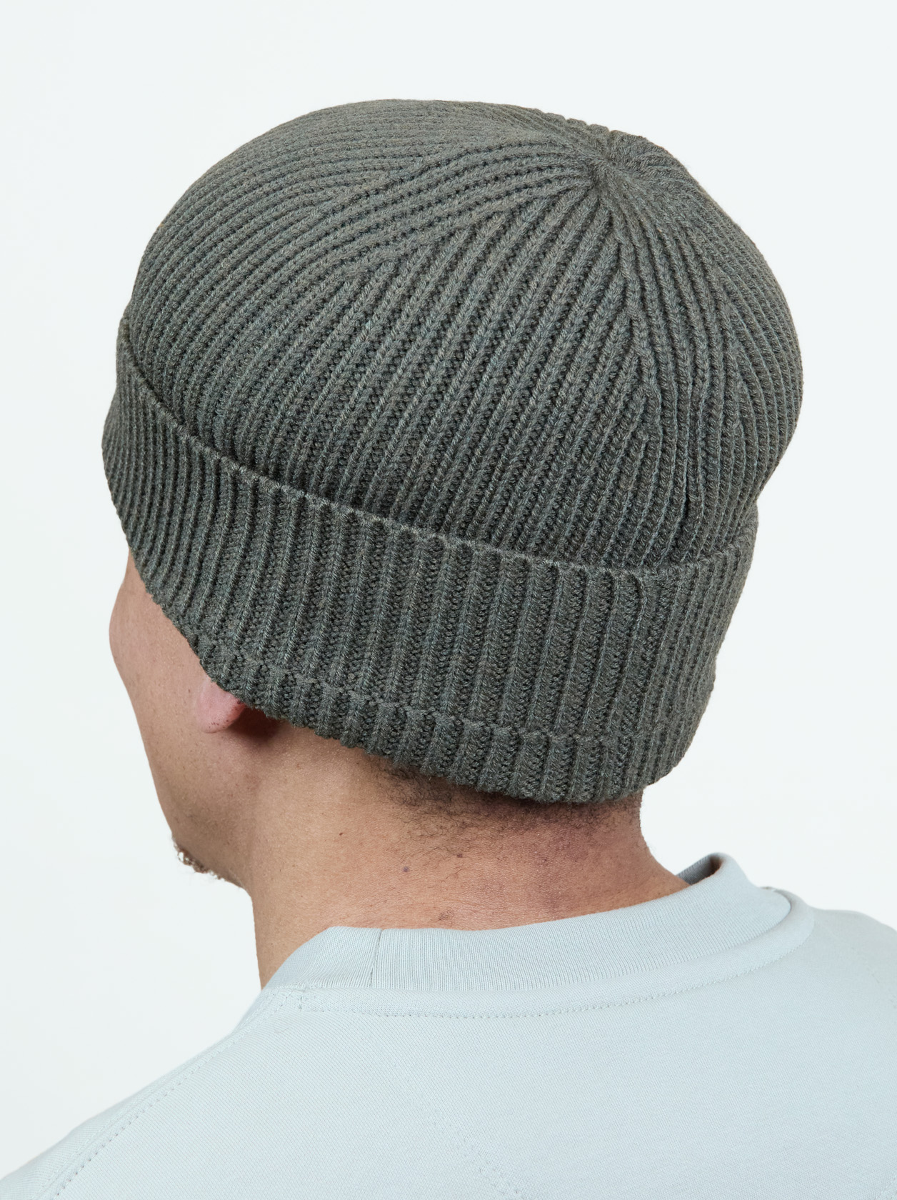 Person wearing a ribbed, gray knit beanie, viewed from the back against a plain background.