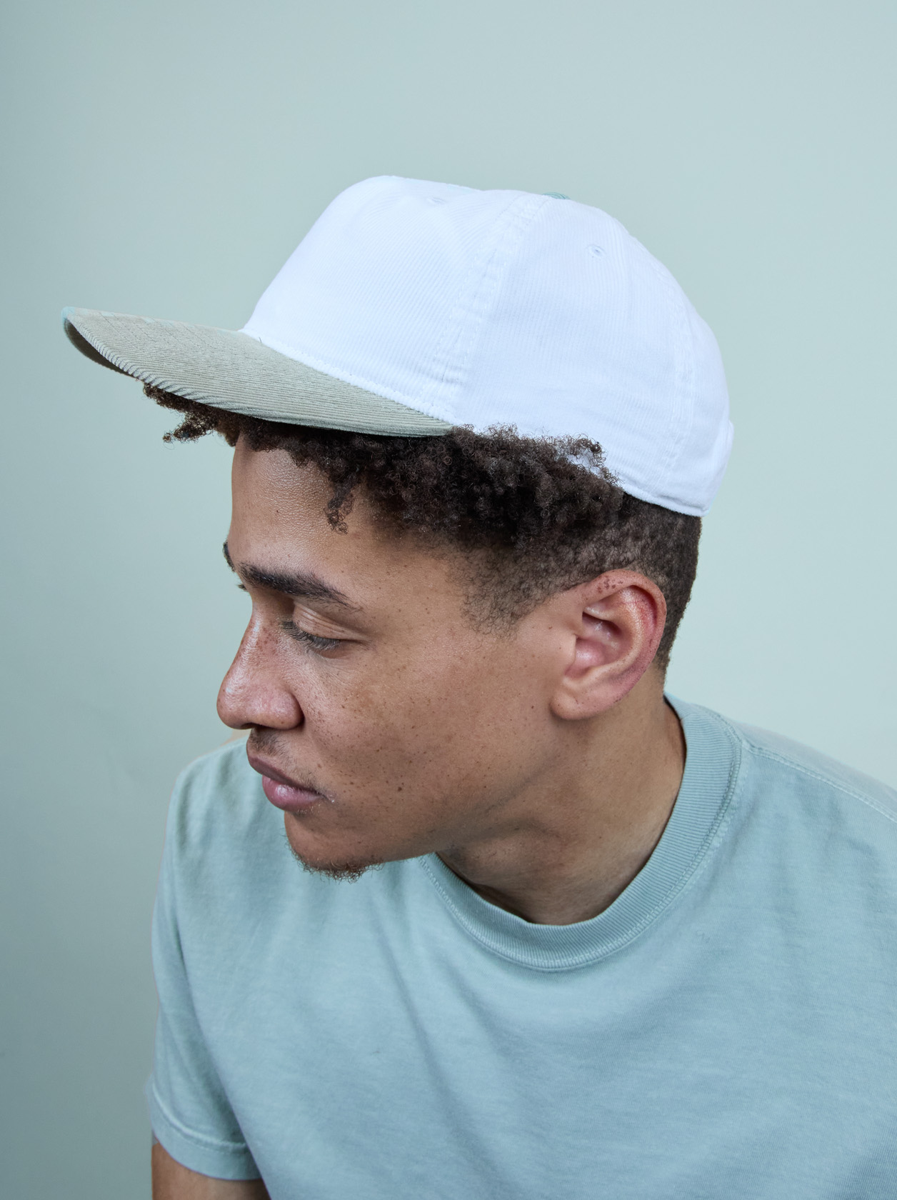 Man in a light blue shirt and white cap looking down against a plain background.