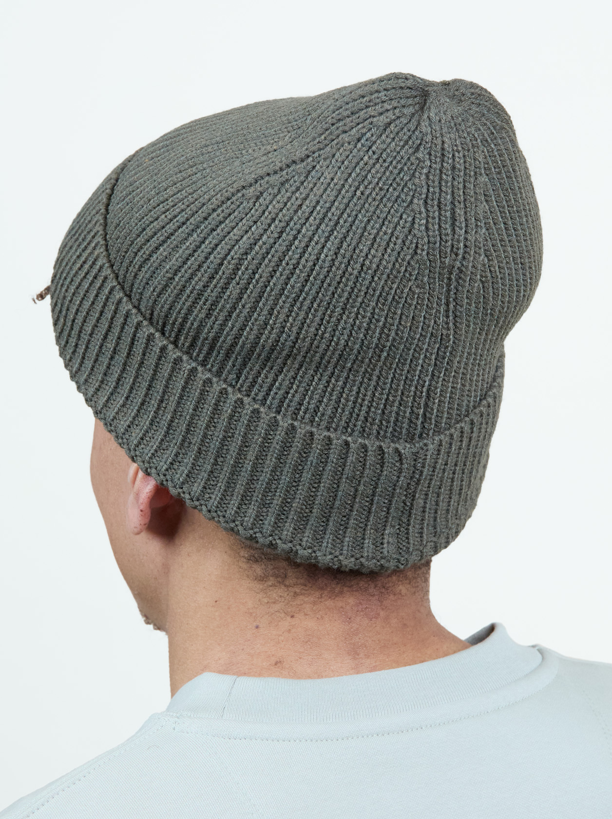 Person wearing a gray knit beanie viewed from behind, with a light-colored shirt against a plain white background.