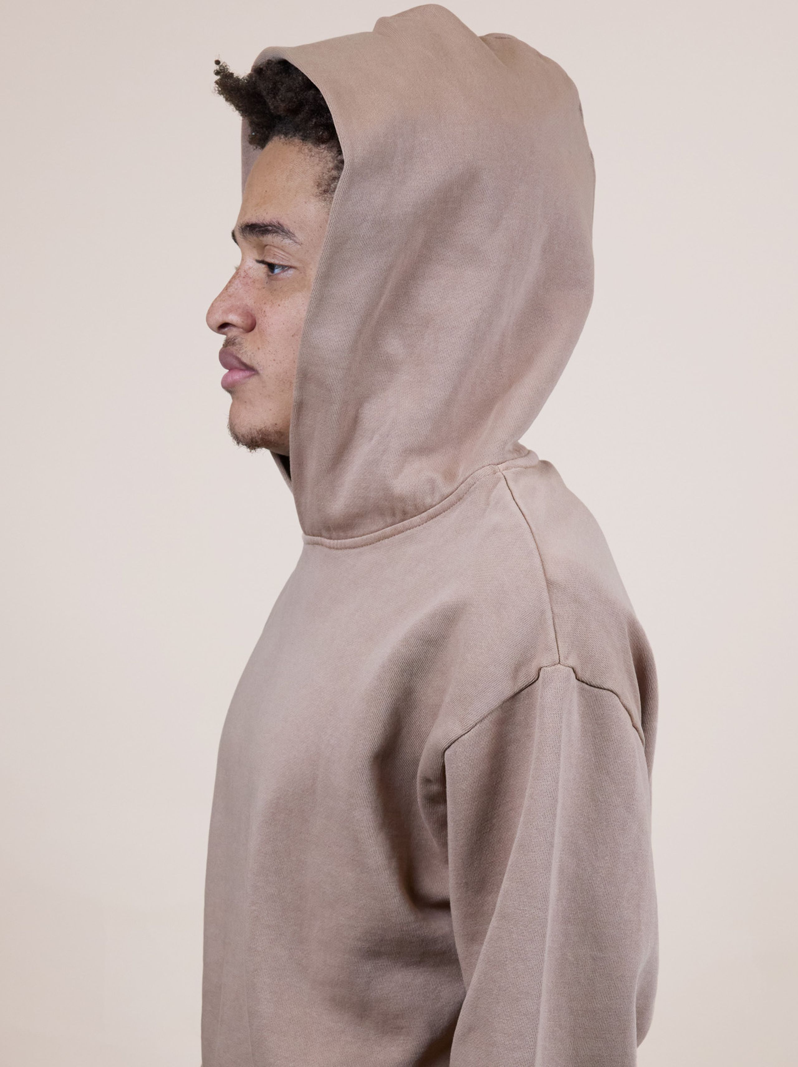 Person in a brown hoodie facing left, looking forward, against a plain background.