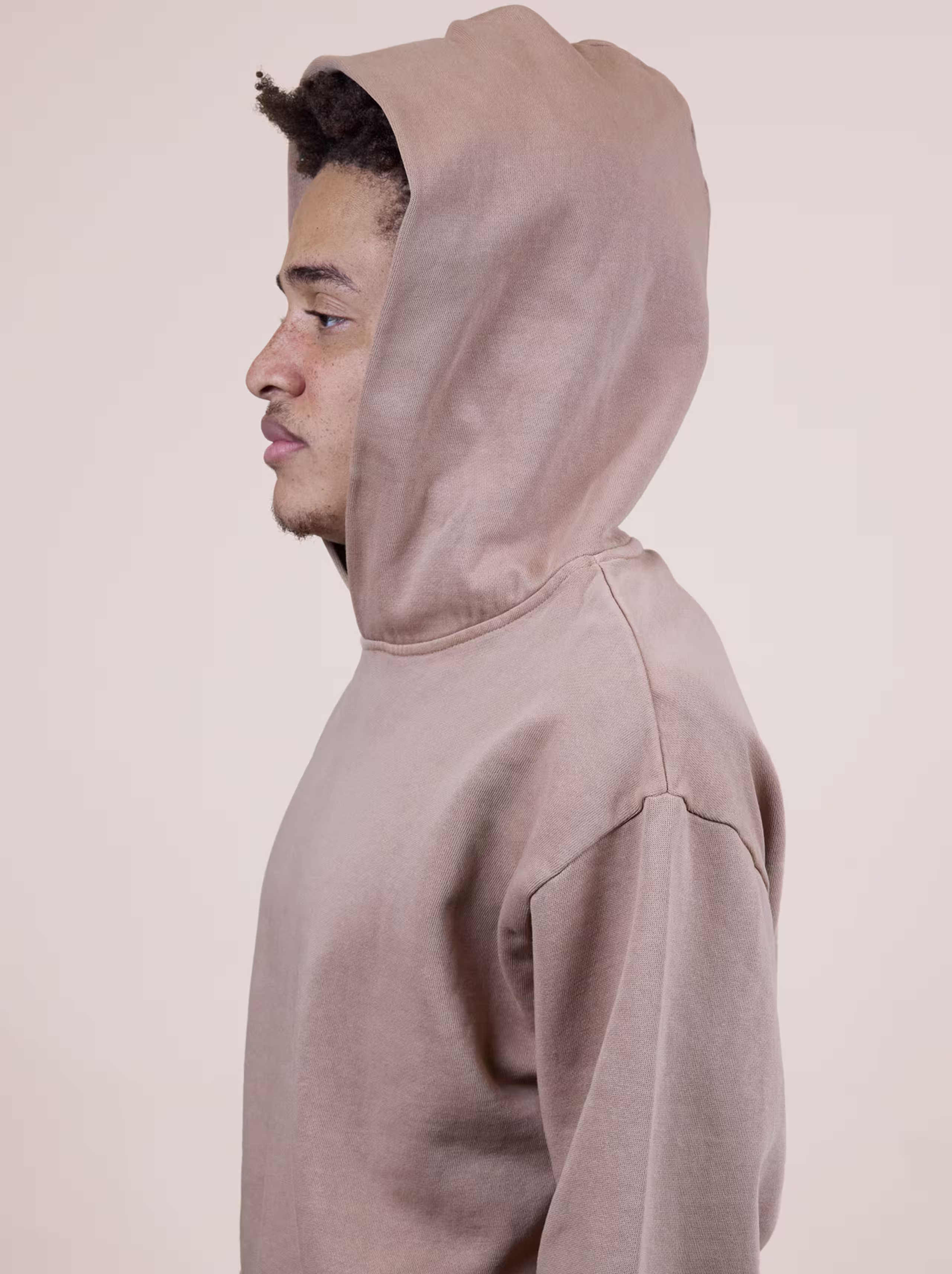 Person in a brown hoodie facing left, looking forward, against a plain background.