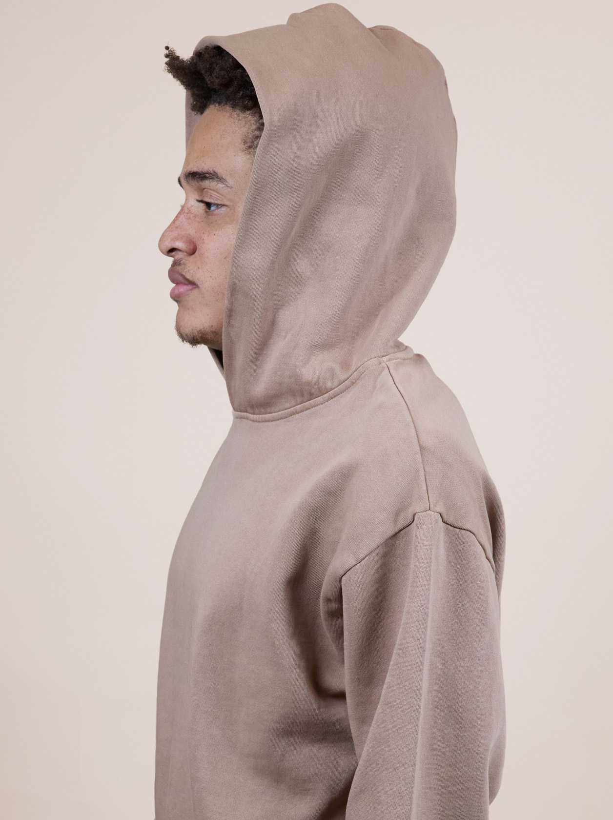 Person in a brown hoodie facing left, looking forward, against a plain background.
