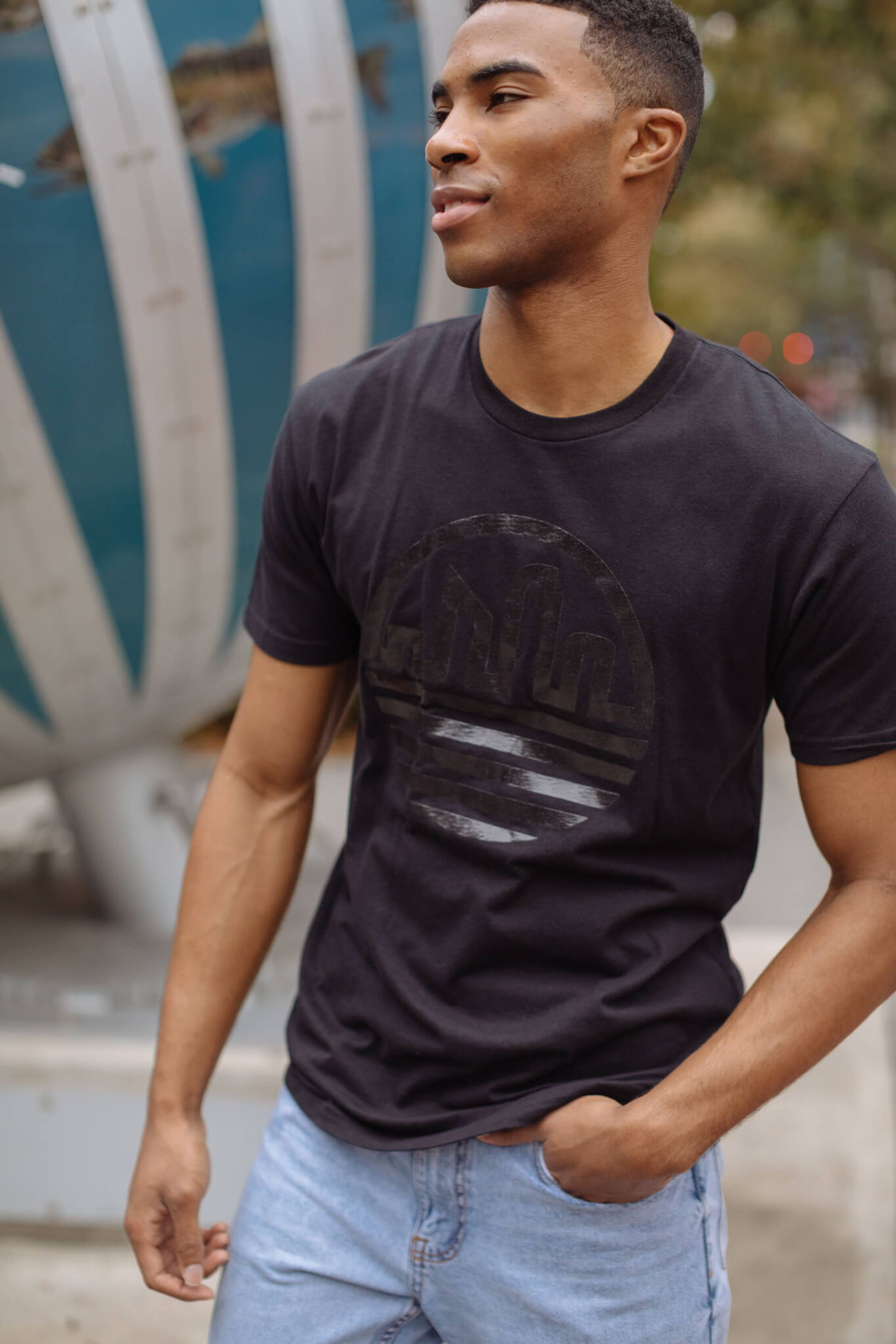 A man wears a black t-shirt with a black metallic printed design 