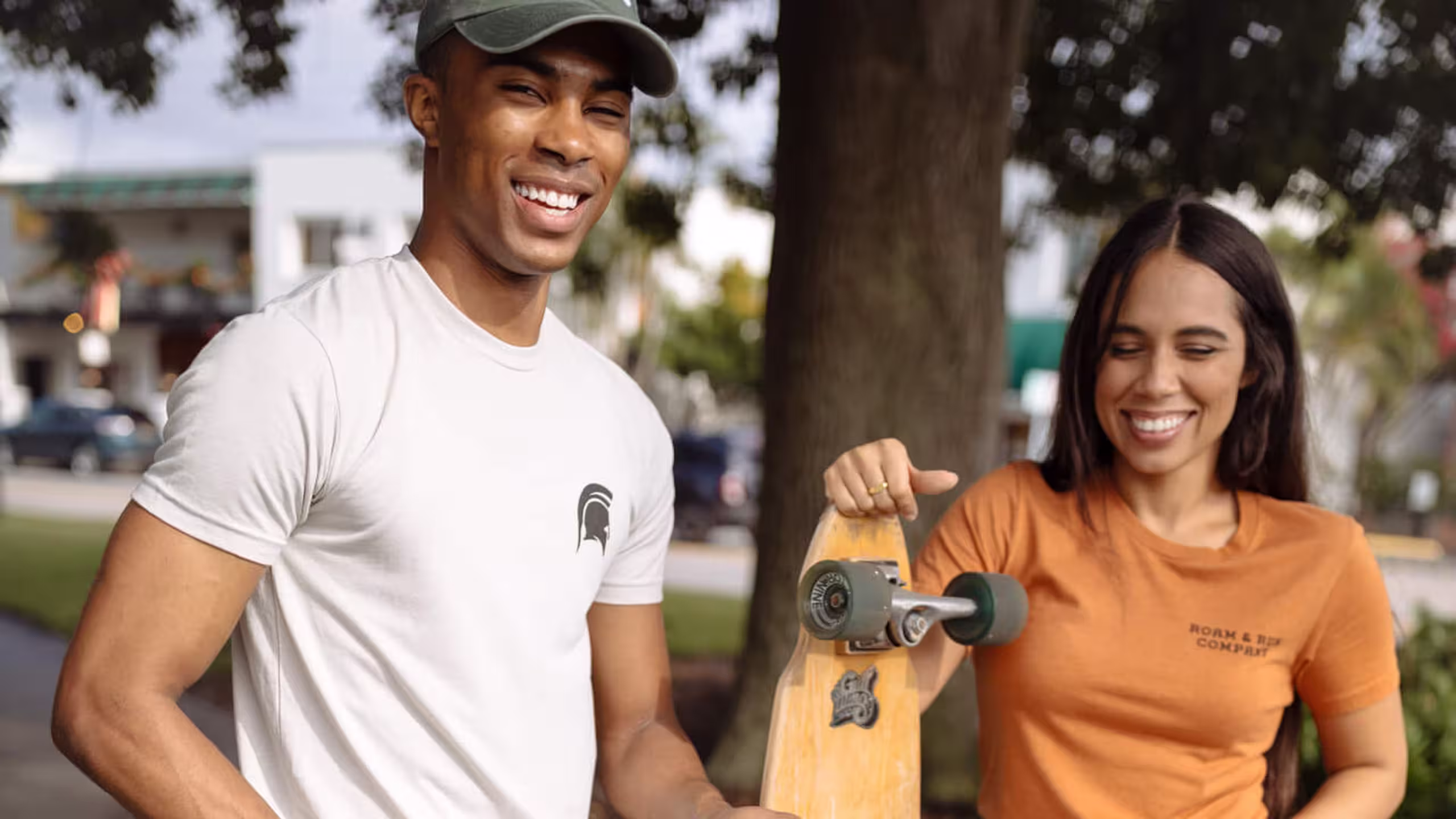 man and women smiling with long-board skateboards