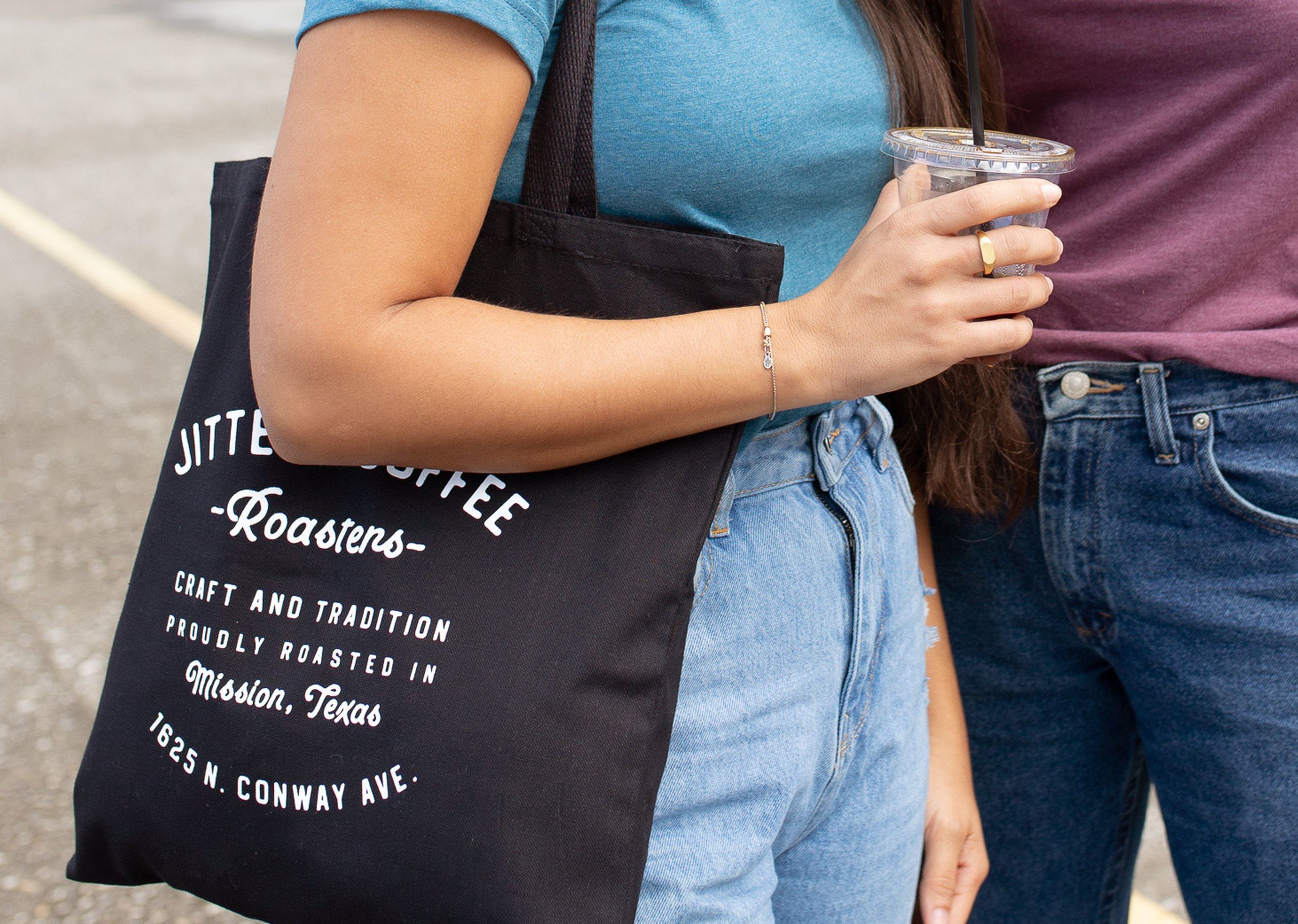 A woman wears a coffee tote bag while holding a cup on the go 