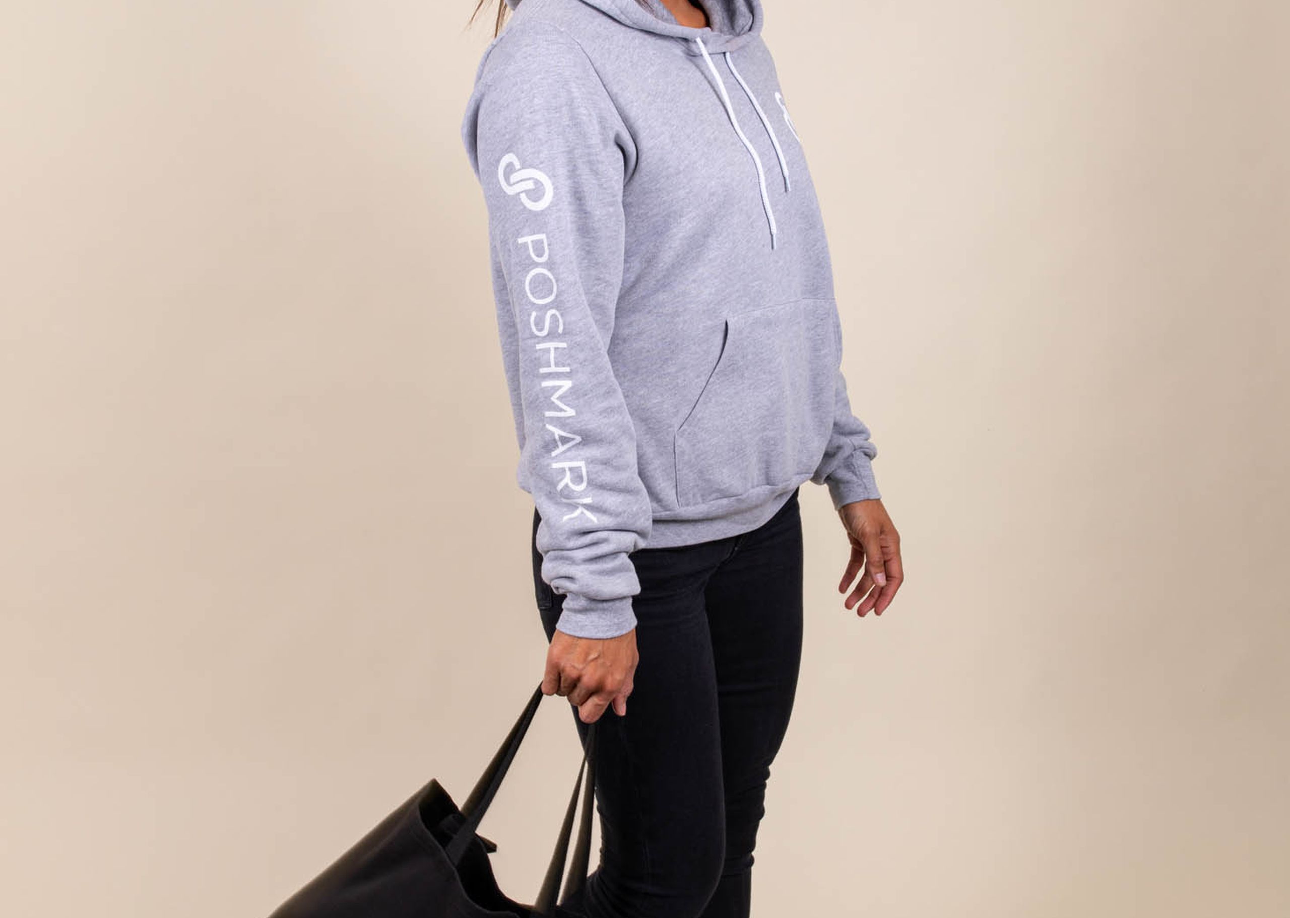 A woman wears a Poshmark sweatshirt and a matching Poshmark tote bag