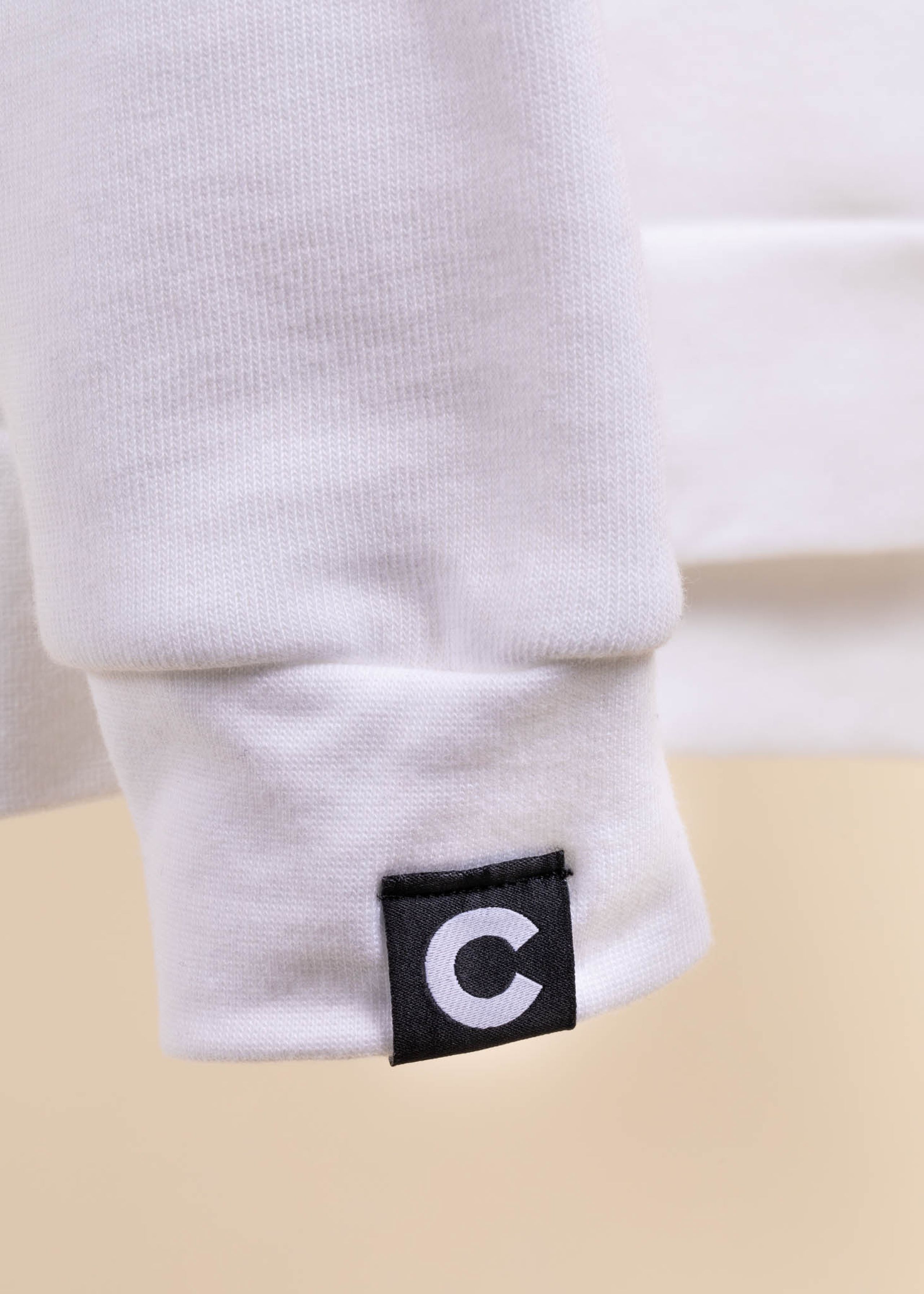 A black hem tag with a white "c" on it is attached to the sleeve of a white sweatshirt