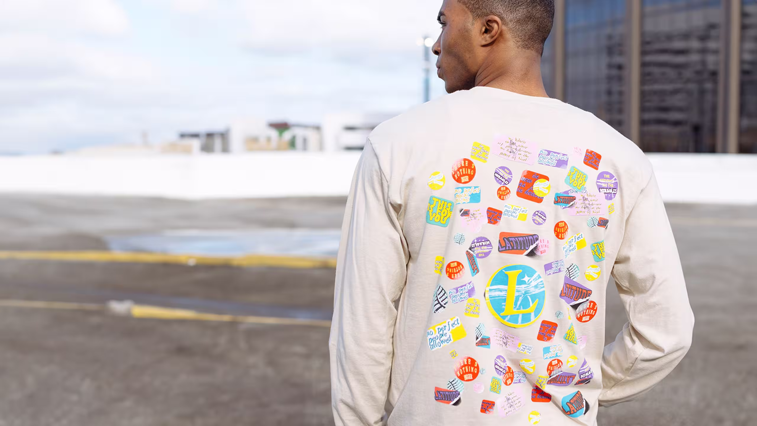 man wearing a light tan color long sleeve t-shirt with puff print sticker graphics printed on it