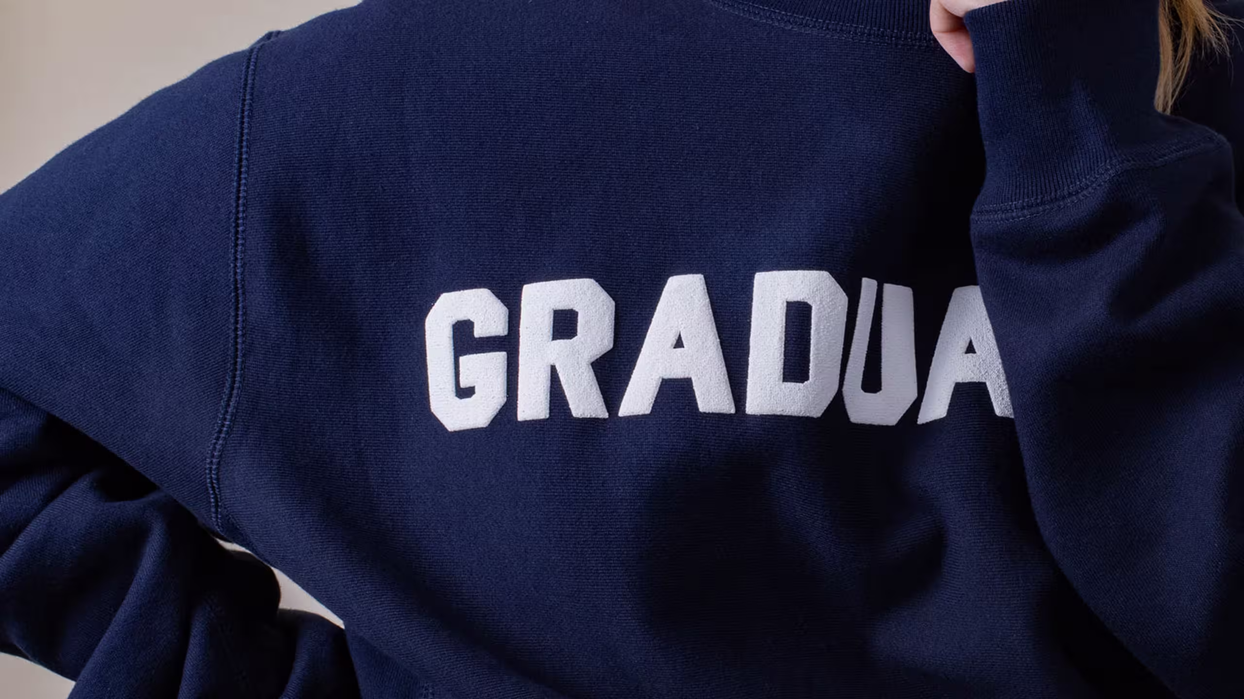 Close up a puff print on a navy hoodie. The letters G, R, A, D, and U are visible. 