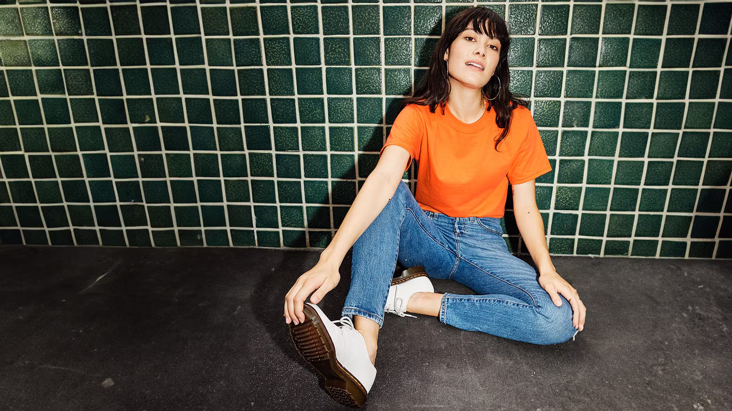 women wearing a orange shirt in front of a dark green tile wall