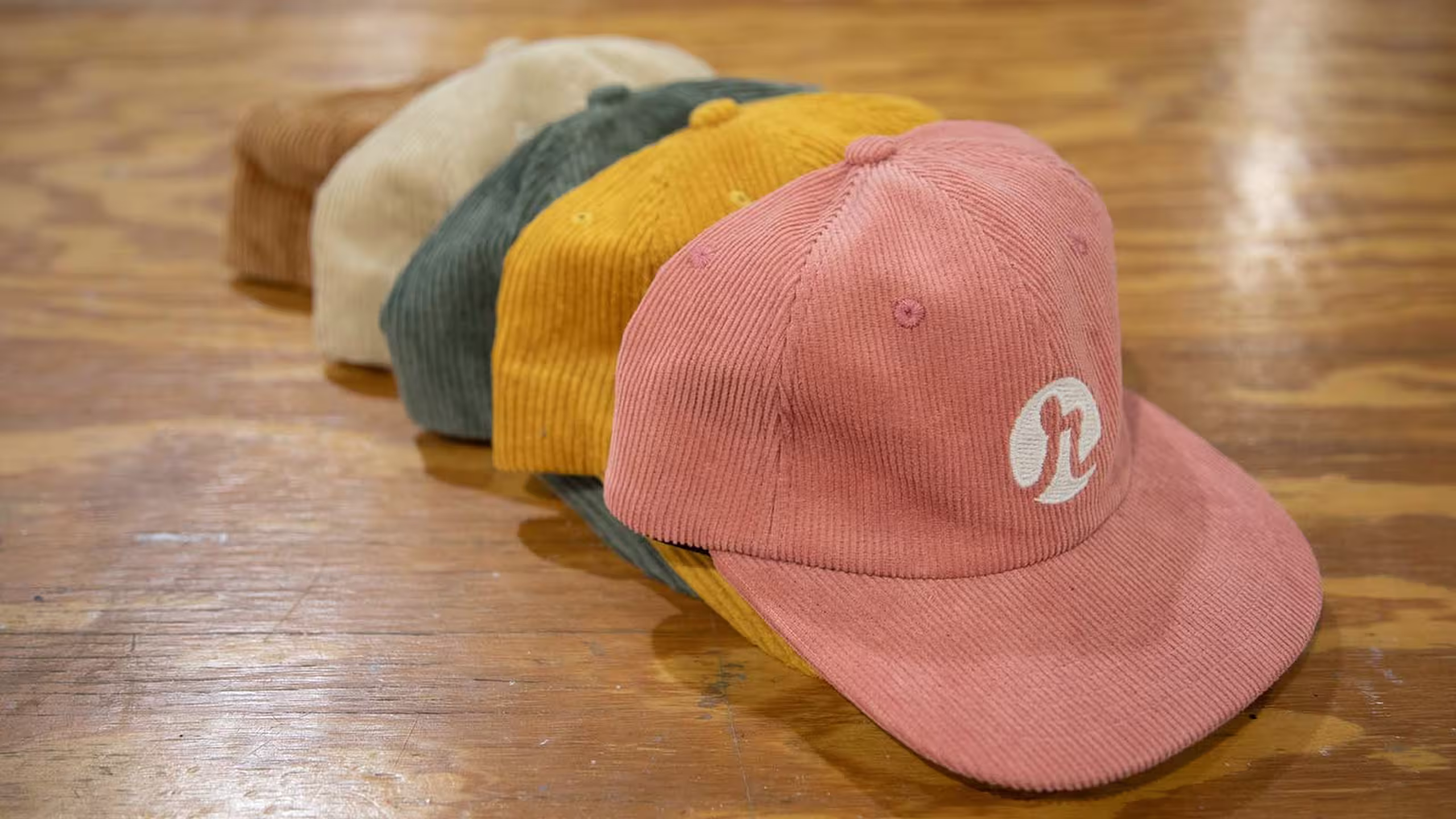 A stack of hats on a wood table. Brown, white, dark green, yellow, and pink from back to front
